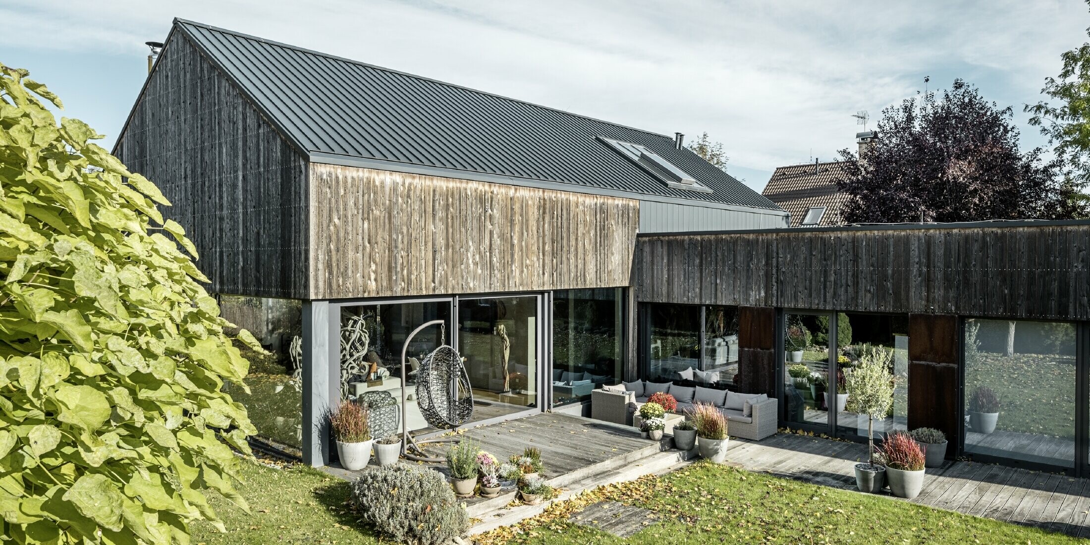 Eengezinswoning met zadeldak, bekleed met dubbele staande fels PREFALZ in antraciet en verweerde houten gevel. Met mooi houten terras en grote raampartijen op de benedenverdieping.