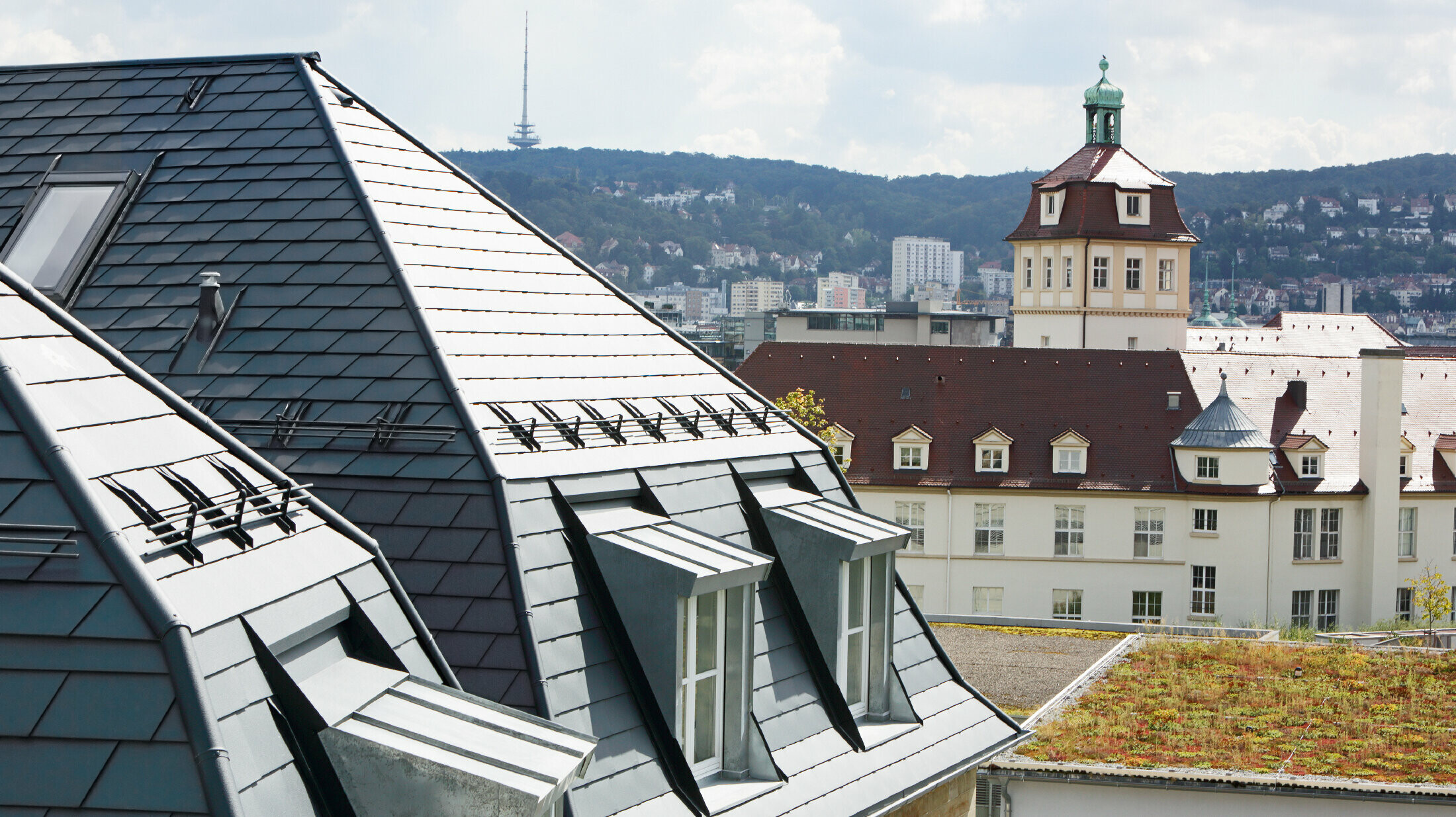 Oud stadshuis in Stuttgart met geknikt dak en veel dakkapellen, bedekt met de aluminium schindels van PREFA in P.10 antraciet