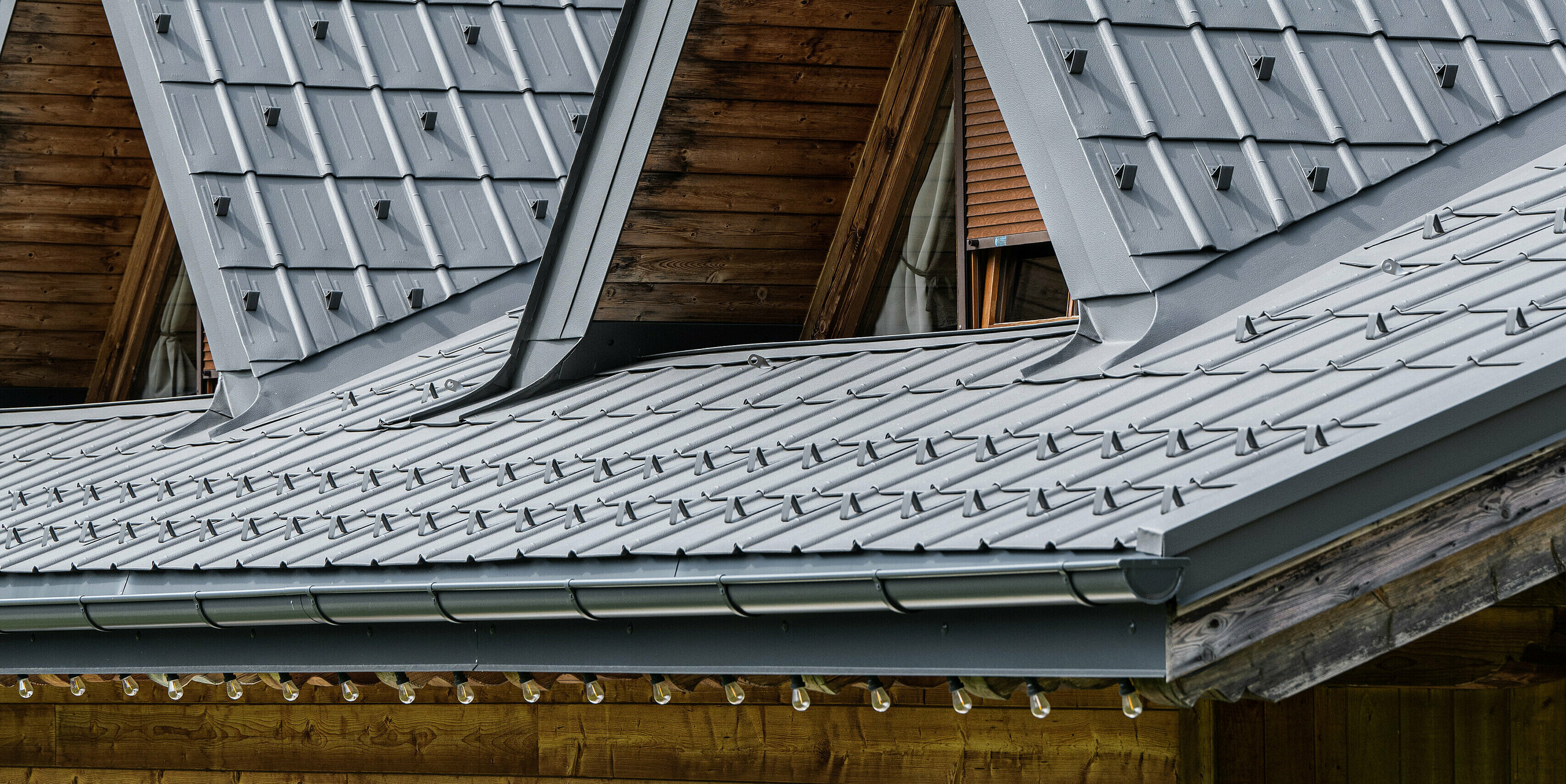 Nahaufnahme eines typischen Alpenhauses in Auronzo di Cadore mit PREFA Dachsystem. Das Dach mit Spitzgauben wurde mit robusten Blechziegeln eingedeckt. Die PREFA Aluminiumprodukte spiegeln die hochwertige und langlebige Konstruktion wider, die sich in die bewaldete Bergkulisse einfügt. Das Dach zeigt eine perfekte Harmonie zwischen traditioneller alpiner Holzbauweise und zeitgemäßer Dacheindeckung, die sowohl funktional als auch optisch beeindruckend ist.