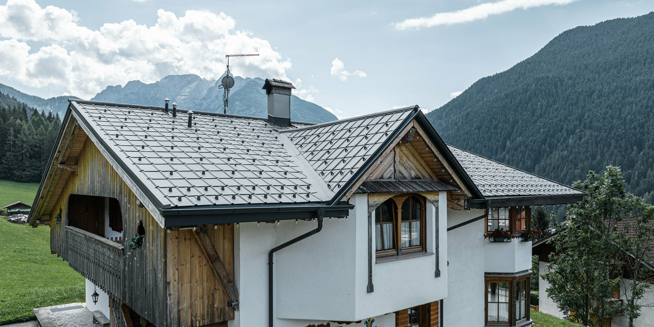 Bergchalet in Auronzo di Cadore, Italien, mit einem frisch renovierten Dach aus hellgrauen PREFA-Ziegeln, das Tradition und Moderne verbindet. Bei der sorgfältigen Restaurierung blieben charmante Details wie Holzbalkone und Schnitzereien erhalten, während das Gebäude durch ein langlebiges, wartungsarmes Aluminiumdach geschützt wurde, das sich in die natürliche Berglandschaft einfügt.