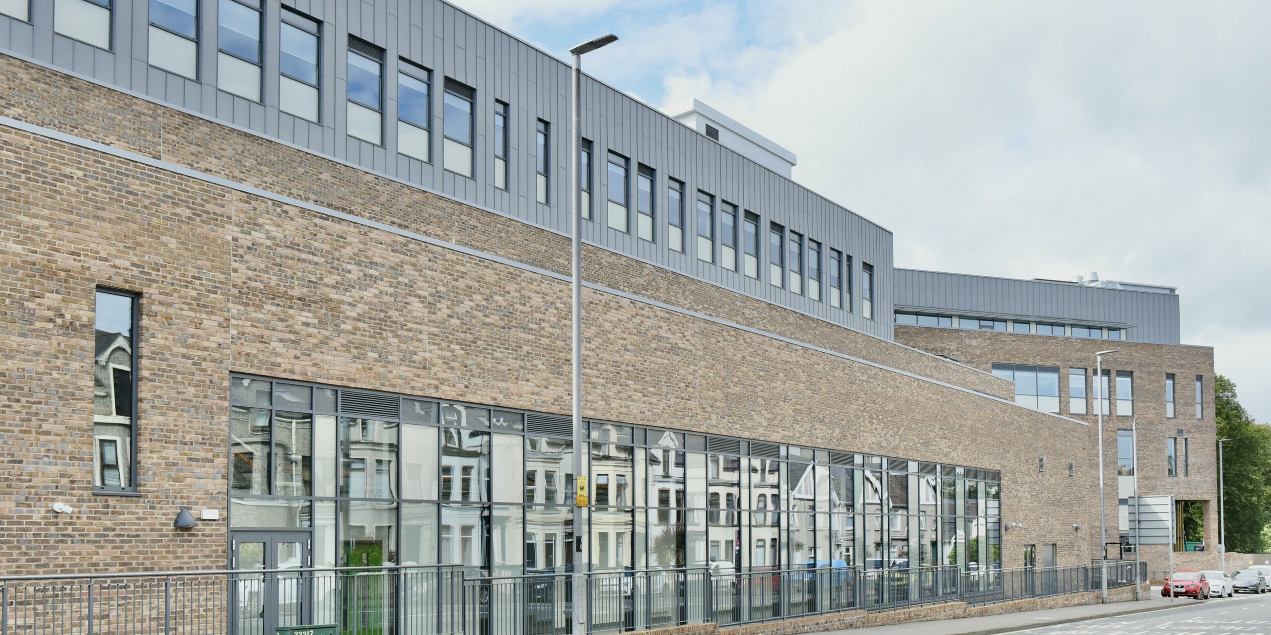 Straßenansicht des North Regional College in Coleraine, Nordirland. Die präzise verarbeitete PREFALZ Aluminiumfassade in Patinagrau ergänzt die traditionelle Architektur und harmoniert mit der klassischen Backsteinoptik. Funktionalität und Design verbinden sich zu einem beeindruckenden Bauwerk.