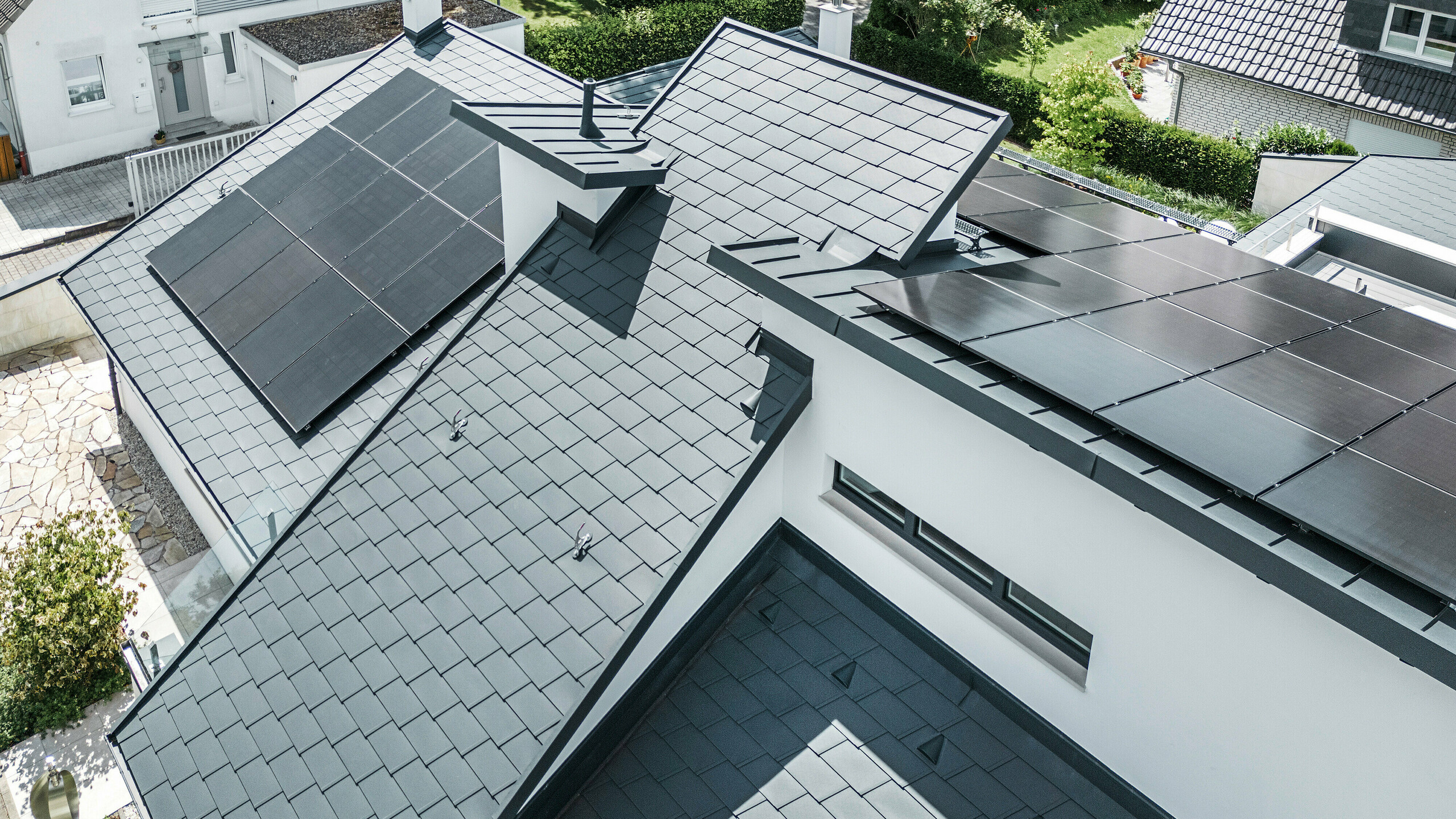 Modern vrijstaand huis in Dortmund met een geavanceerd fotovoltaïsch systeem, geïnstalleerd op een PREFA daksysteem bestaande uit DS.19 dakshingles en PREFALZ felsbanen in de kleur P.10 antraciet. De montage van het PV-systeem vindt plaats met Vario-zonnepaneelbeugels voor de dakshingles en PREFALZ Vario-zonnepaneelbeugels voor de felsbanen. Het zonnesysteem zorgt voor een efficiënte energieopwekking uit hernieuwbare energiebronnen. Het geraffineerde dakdesign biedt een optimale balans tussen esthetiek en functionaliteit.  Vertaald met DeepL.com (gratis versie)