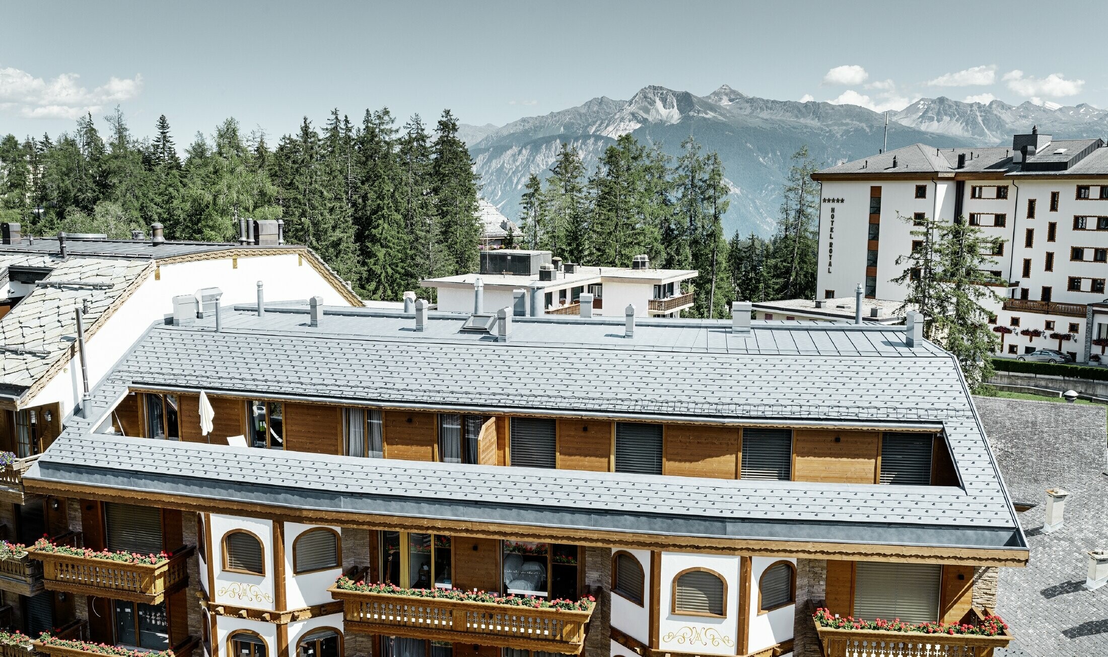 Meergezinswoning in Crans Montana (Zwitserland) met de bergen als decor, een gevel met speelse houten elementen en een dakbedekking bestaande uit aluminium PREFA-dakschindels in steengrijs