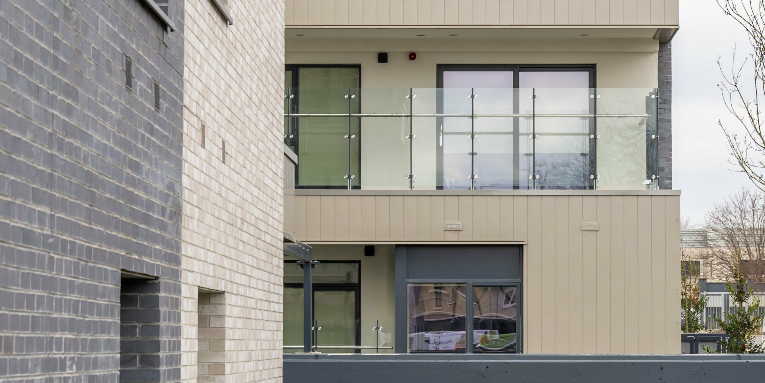 Detailansicht der Fassade des Palmers Gate Wohnkomplexes in Palmerstown, Dublin, Irland. Das Bild zeigt die Kombination von bronzefarbenen PREFA Aluminiumprodukten und Ziegelsteinelementen. Die Balkone sind mit Glasgeländern ausgestattet und bieten moderne Wohnqualität. Die Außenhüllen bestehen aus etwa 1.700 m² PREFA Sidings und ca. 1.200 m² PREFALZ Fassadensystem. Das Bild hebt die architektonischen Details und die hochwertige Materialwahl hervor, die zur ästhetischen und funktionalen Gestaltung der Gebäude beiträgt.