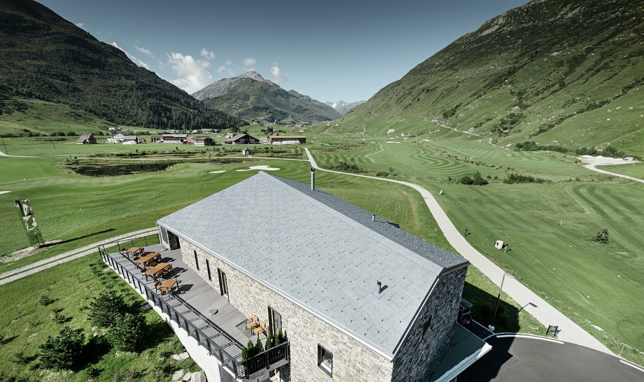 Modern clubhuis van golfterrein in Andermatt (Zwitserland) met gevel in natuursteen en aluminium FX.12 dakpanelen in steengrijs van PREFA 