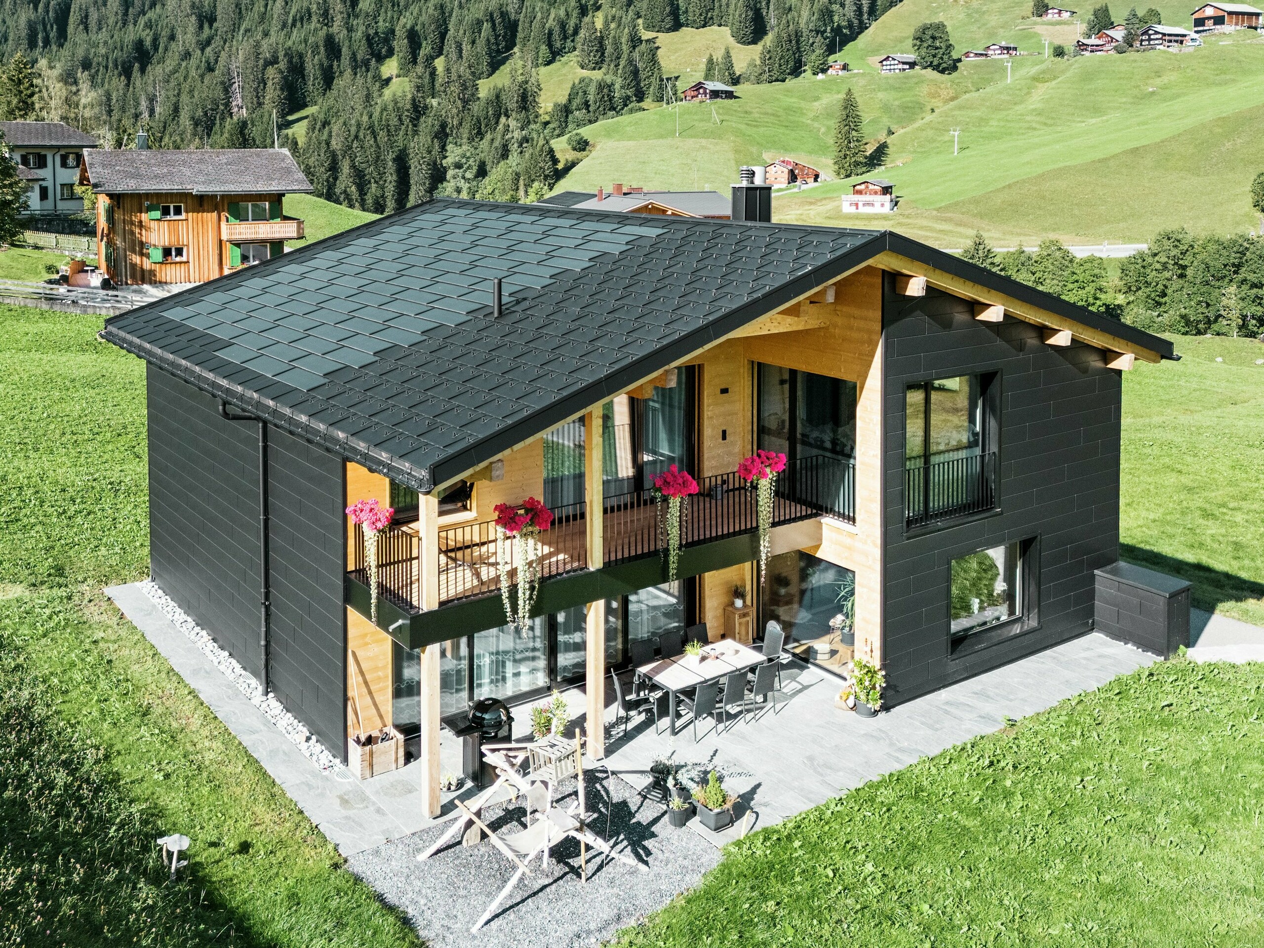 Het elegante vrijstaande huis in de heuvelachtige omgeving van Ascharina (Zwitserland) laat zien hoe aluminium en hout perfect gecombineerd kunnen worden. De robuuste PREFA Siding.X gevelplaten in P.10 zwart harmoniëren met het dak van PREFA Solar dakplaten en R.16 dakplaten in dezelfde kleurcoating. De duurzame aluminium gevelbekleding beschermt het gebouw betrouwbaar tegen de uitdagingen van het alpine klimaat.