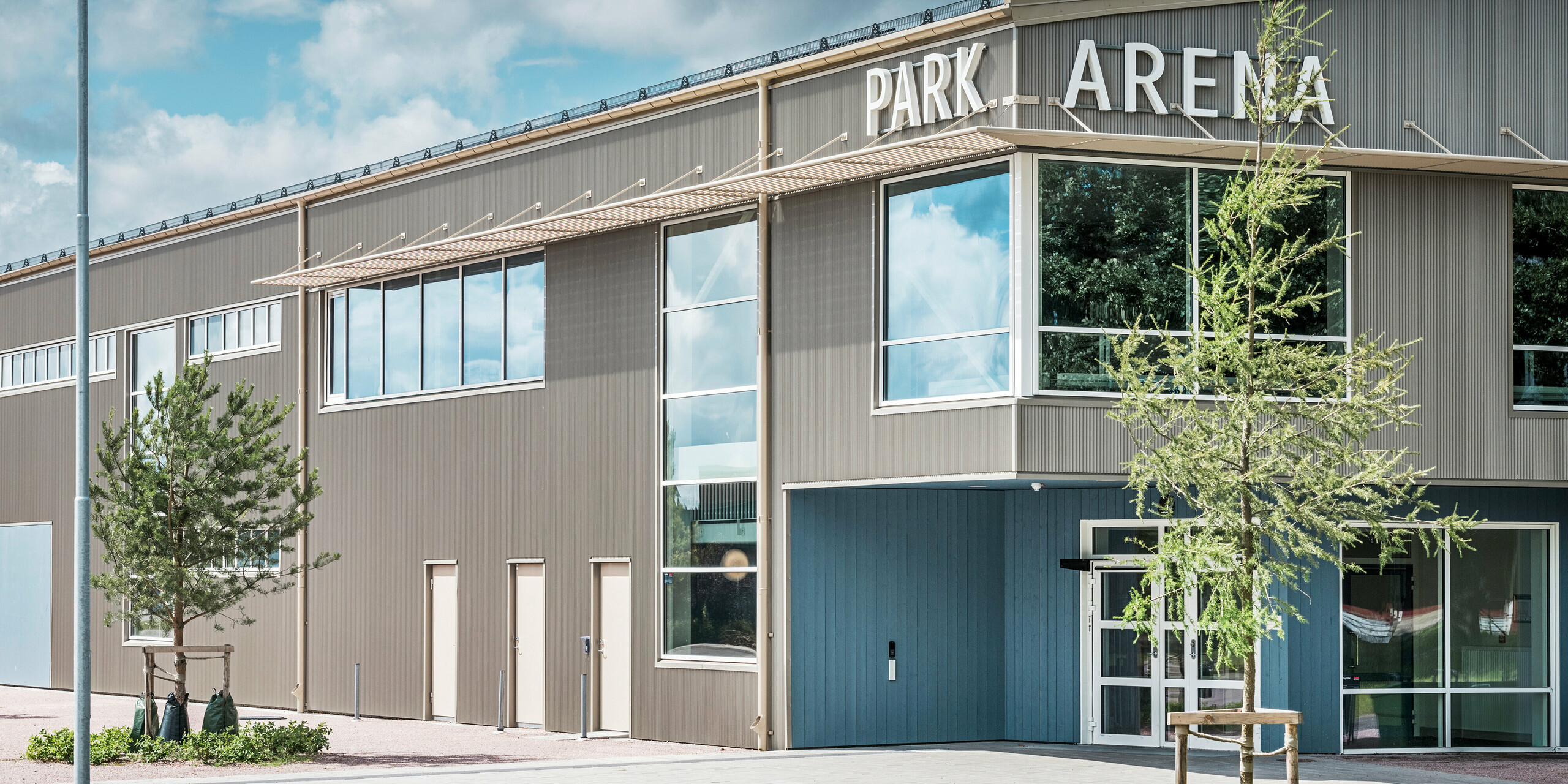 Eingangsbereich der Park Arena in Värnamo, Schweden, mit moderner Fassadengestaltung in Form des stranggepressten PREFA Zackenprofils in Bronze. Die langlebige und witterungsbeständige Aluminium-Fassade verleiht der 3.300 m² großen Sporthalle ein elegantes und markantes Erscheinungsbild. Das PREFA Zackenprofil sorgt für faszinierende Licht- und Schatteneffekte, die das architektonische Design der Arena hervorheben.