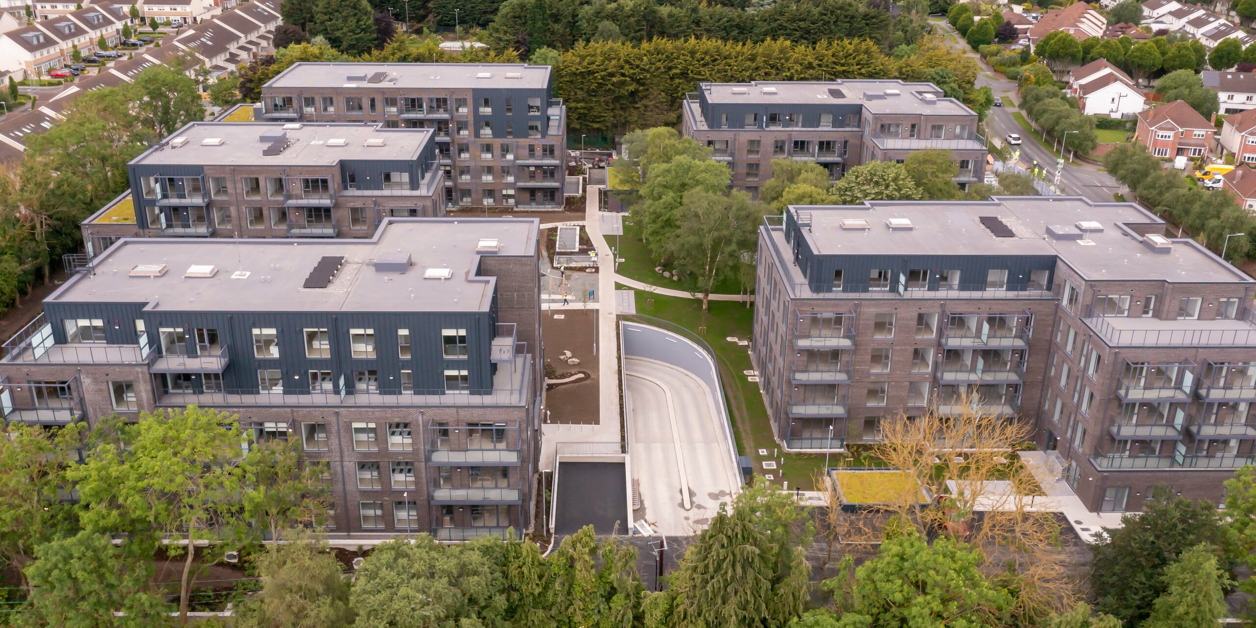 Panoramaansicht der Wohnanlage Balroy Hall in Carpenterstown, Dublin. Moderne Architektur kombiniert eine Aluminiumfassade aus PREFALZ in P.10 Anthrazit mit traditionellem Backstein. Die langlebige Metallfassade wurde auf einer Fläche von 800 m² verlegt und veredelt die Gebäude. Das urbane Design harmoniert mit der Umgebung. 