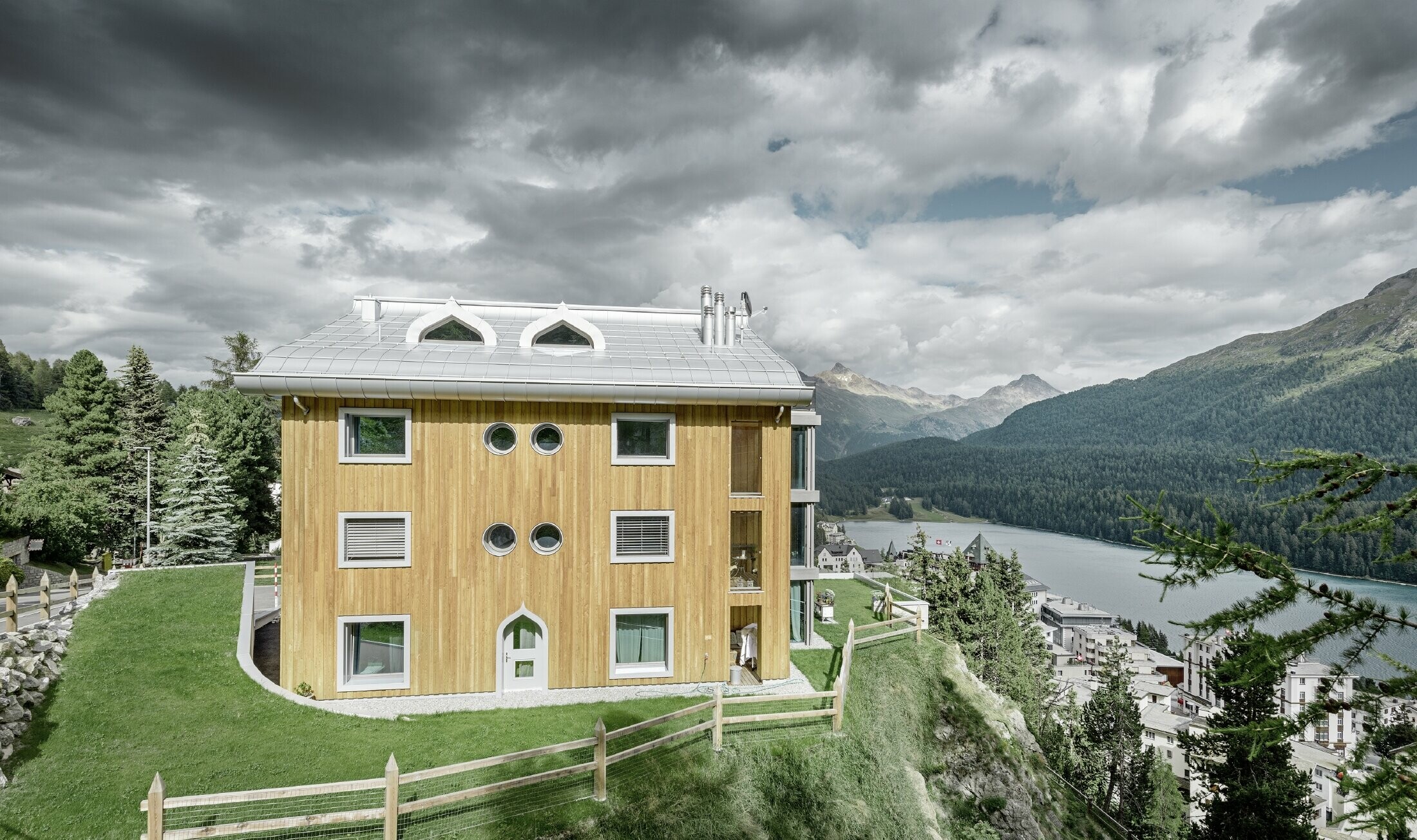 Meergezinswoning in Sankt Moritz (Zwitserland) met houten gevel en aluminiumdak met gekromde dakrand in zilver metallic