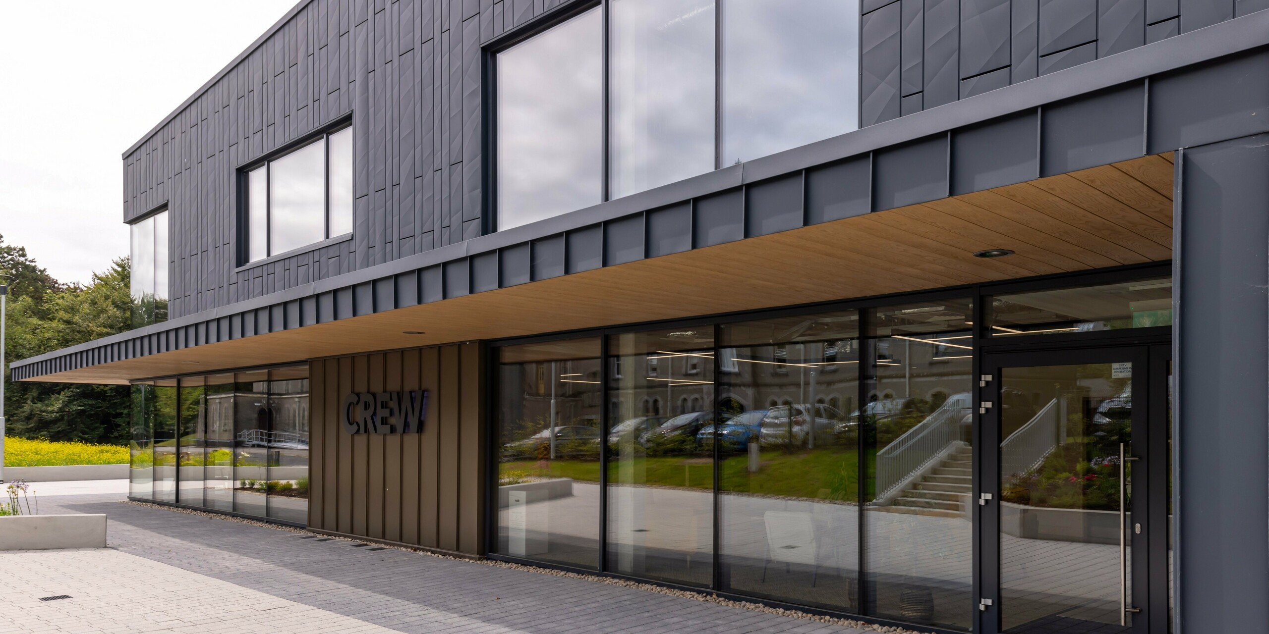 Moderne Fassade des CREW-Gebäudes in Galway, Irland, gestaltet mit PREFA Siding.X Fassadenpaneelen und PREFALZ in der Farbe P.10 Anthrazit. Die robuste Aluminiumverkleidung verleiht dem Bauwerk eine elegante, zeitgemäße Ästhetik. Klare Linien, großzügige Fensterflächen und hochwertige Materialien unterstreichen die innovative Architektur des Bürozentrums.