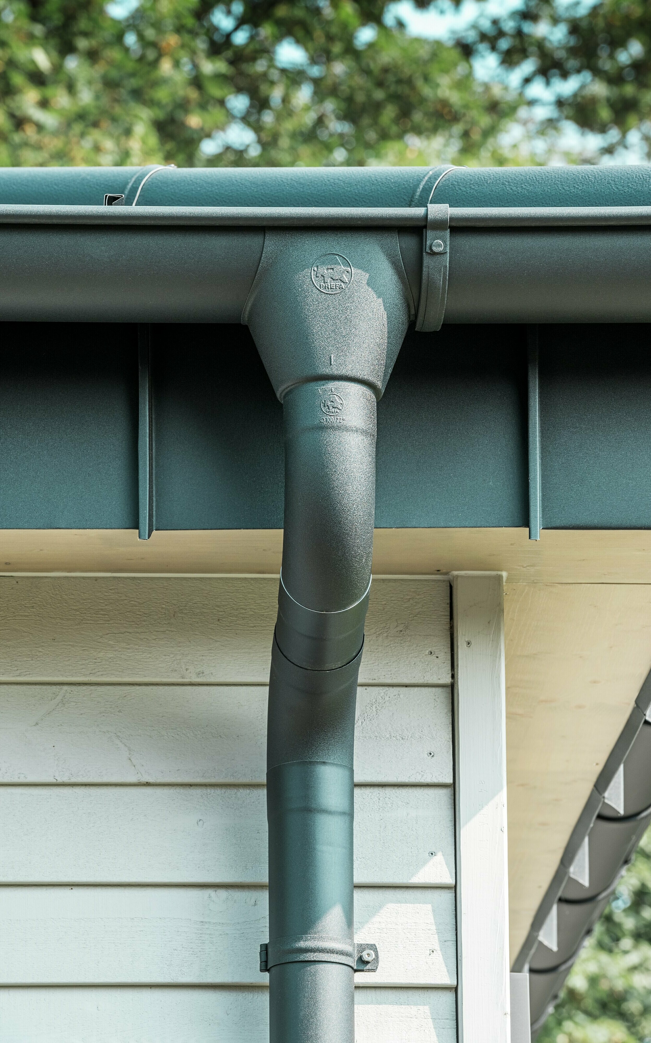 Nahaufnahme der robusten PREFA Dachentwässerung eines Bungalows in Rommerskirchen. Die hochwertige Saumrinne und das Ablaufrohr in P.10 Schwarz bieten optimalen Schutz vor Witterungseinflüssen. Langlebigkeit und Funktionalität verbinden sich hier mit elegantem Design aus Aluminium.