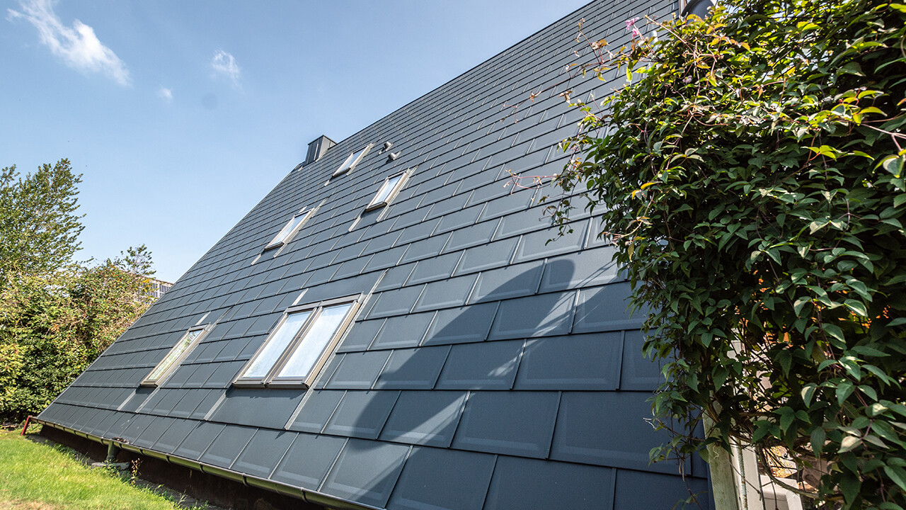 Lang dakvlak van een A-framewoning gedekt met de PREFA dakpan in P.10 antraciet. In het dakvlak zijn een aantal dakramen geplaatst.