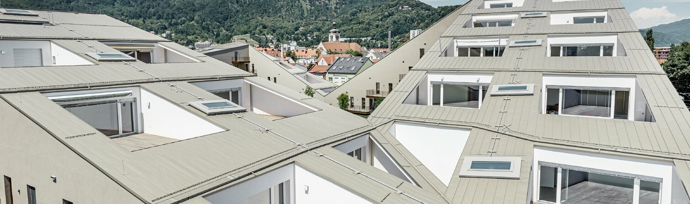 Langgerekt woongebouw in Graz (Oostenrijk) met platte dakvlakken, geïntegreerde terrassen, grote ramen en Prefalz-dak in speciale kleur brons metallic