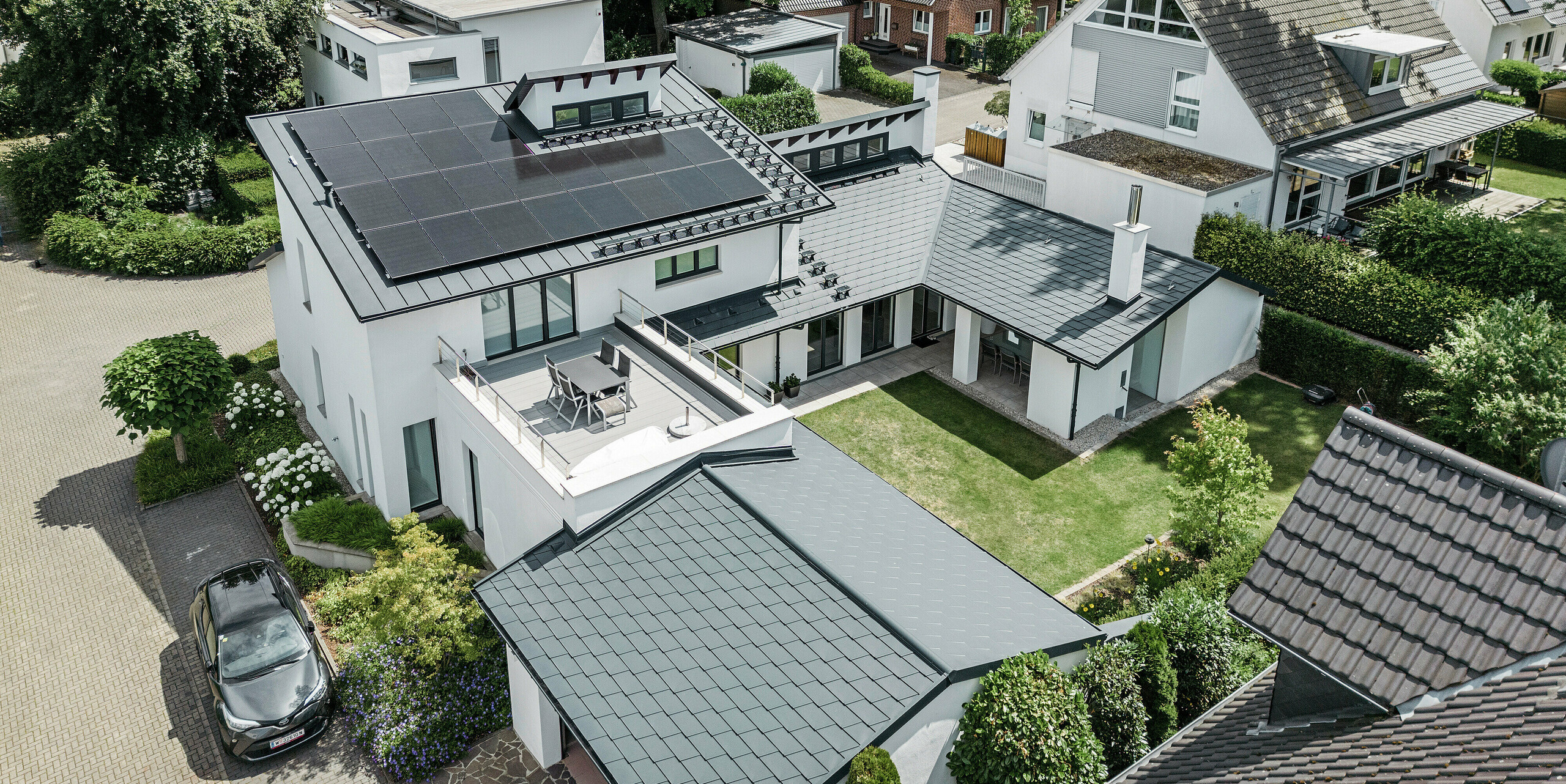 Uitzicht in vogelvlucht op het markante daklandschap van een eengezinswoning in Dortmund met PREFA dakshingles DS.19 en PREFALZ in P.10 antraciet en een grootschalige PV-installatie